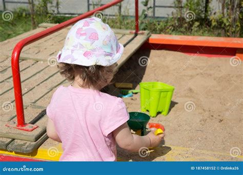 The Little Toddler Girl Plays In The Sandbox In Summer In The City