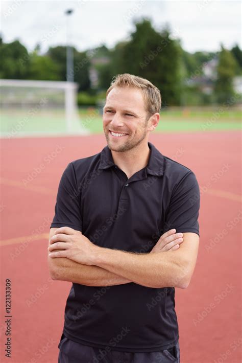 lächelnder mann steht mit verschränkten armen auf dem sportplatz Stock