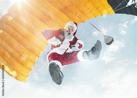 Merry Christmas And Happy Holidays Santa Claus Flying With Parachute Over Background Of Blue