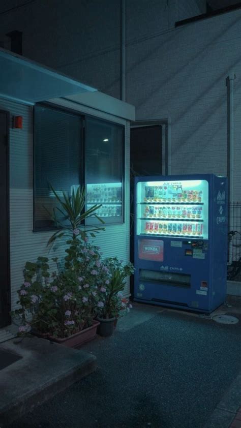 A Vending Machine Sitting In Front Of A Building With Flowers Growing