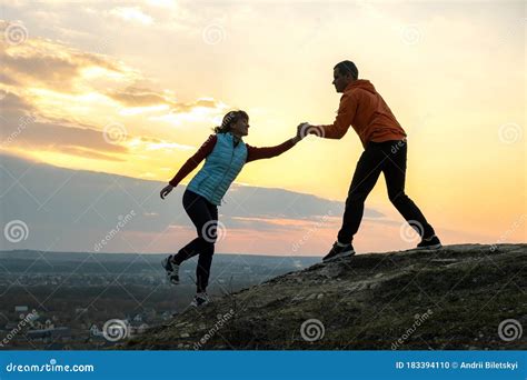 Man And Woman Hikers Helping Each Other To Climb Stone At Sunset In