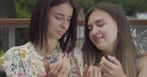 Two Pretty Girls Sitting Outdoors Together Chatting About New Manicure Showing Fingers And