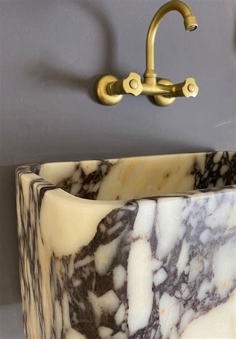 A Marble Sink In A Bathroom Under A Faucet Mounted On The Wall Above It