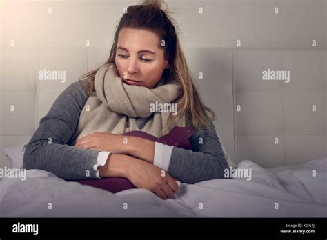 Sick Woman Wrapped In A Warm Scarf And Clutching A Hot Water Bottle