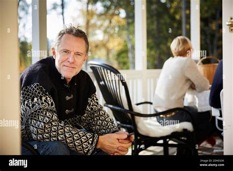 Portrait Of Smiling Mature Man Sitting On Porch With Friend Sitting In