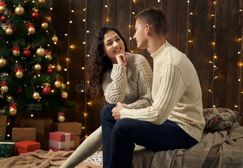 Young Couple In Christmas Lights And Decoration Dressed In White Fir Tree On Dark Wooden