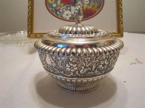 An Ornate Silver Bowl Sits On A Table Next To A Gold Framed Picture And