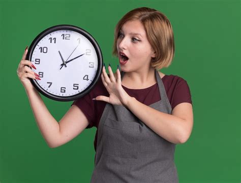 Peluquería de mujer hermosa joven en delantal sosteniendo reloj de