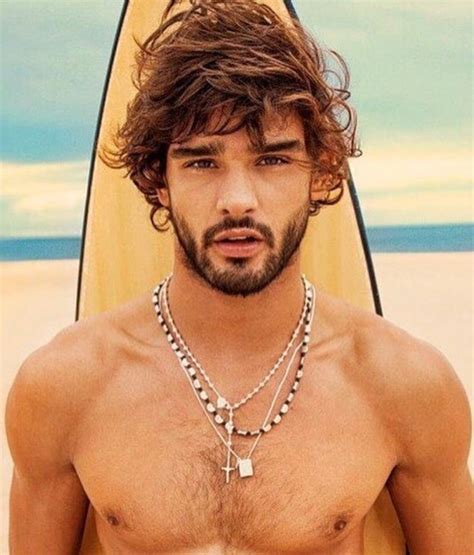 A Shirtless Man Standing On The Beach With His Surfboard In Front Of Him