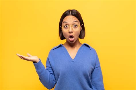 Jovem latina parecendo surpresa e chocada o queixo caído segurando