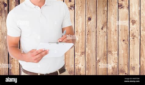 Delivery Man Writing On Clipboard Against Wooden Background Stock Photo