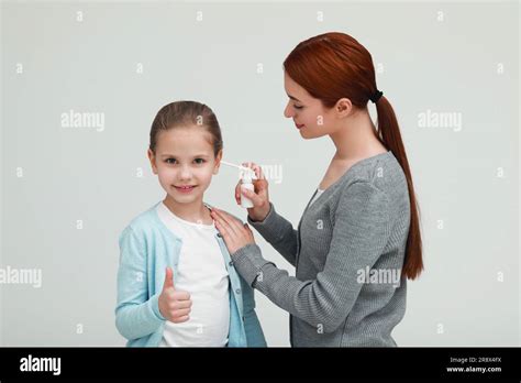 Mother Spraying Medication Into Daughters Ear On Light Grey Background