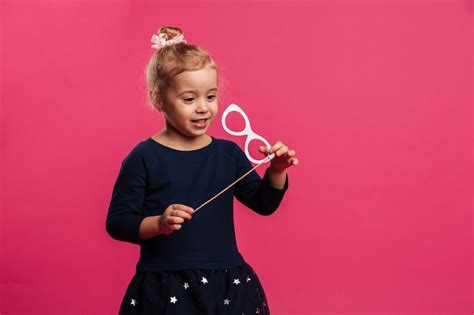 Heureuse Jeune Fille Blonde Jouant Avec Des Lunettes En Papier Sur Le Mur Rose Photo Gratuite