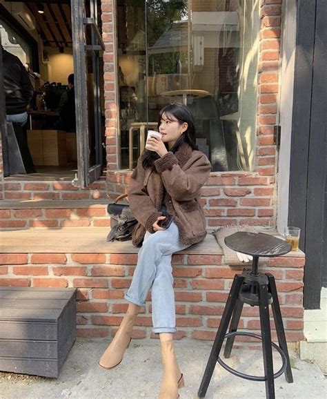 A Woman Sitting On A Brick Wall Drinking From A Cup While Looking Out