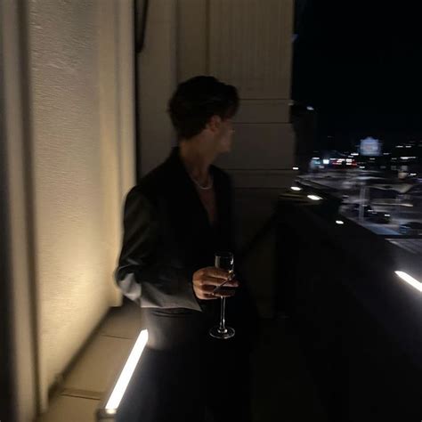 A Woman Holding A Wine Glass On Top Of A Balcony At Night With City