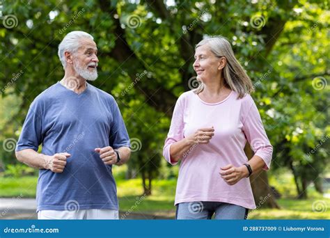 Senior Couple Of Pensioners Jogging In The Park Gray Haired Man And