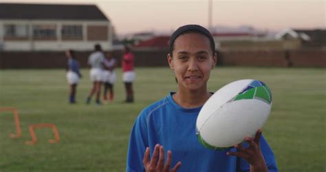 Portrait Of Happy Biracial Female Rugby Player Holding Rugby Ball On