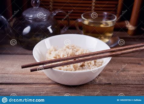 Arroz Moreno Cocinado En El Cuenco Blanco Con Los Palillos En El Fondo