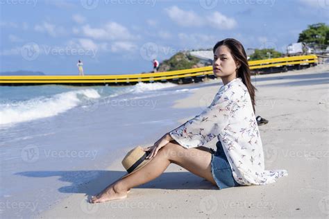 Worried woman sitting on beach with a straw hat on her knees tropical beach by the sea in sunny ...