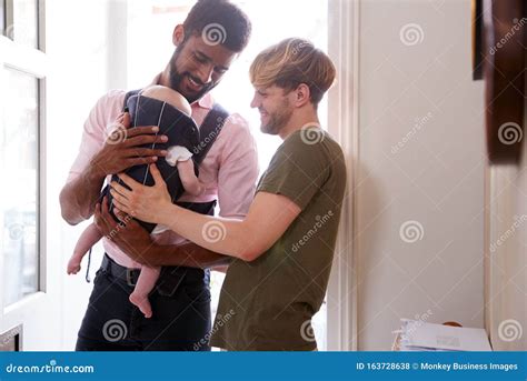 Same Sex Male Couple With Baby Daughter In Sling Opening Front Door Of