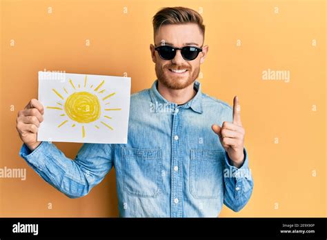 Young Redhead Man Holding Sun Draw Wearing Sunglasses Smiling With An