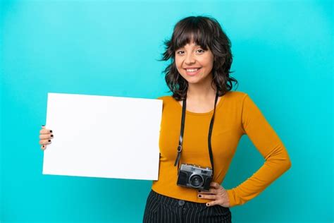 Jovem fotógrafa latina isolada em fundo azul segurando um cartaz vazio expressão feliz