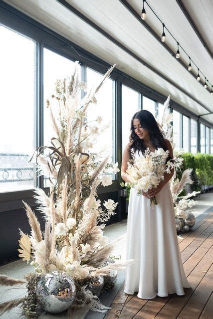 A Woman In A White Dress Is Standing Next To Some Tall Plants And