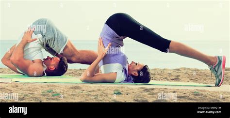 Young couple doing yoga poses sitting on sunny beach by ocean in ...