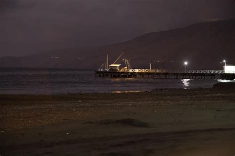 Premium Photo | A pier on the beach at night with a mountain in the ...