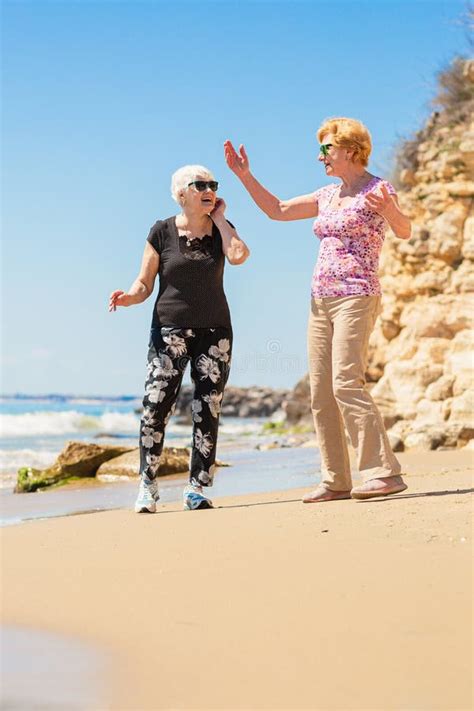 Two Senior Women Walking Along The Rocky Seashore Stock Image Image