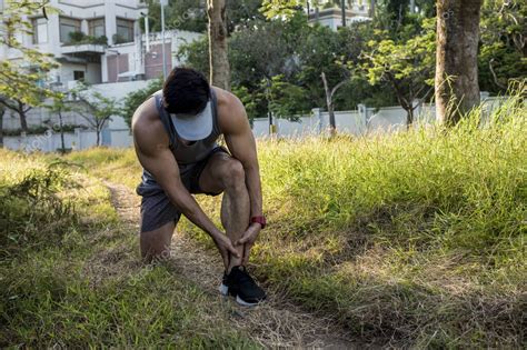 Un corredor asiático se detiene y masajea su pierna para aliviar el