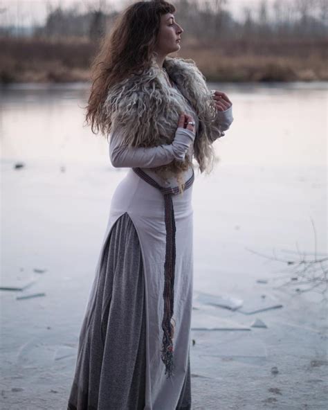 a woman in a long dress and fur vest standing on ice with her arms around her waist