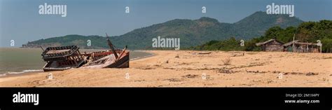 Fishing Boat Wreck On A Beach With Hills And Huts In A Background Stock