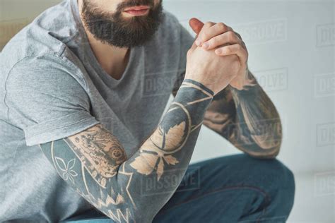 Cropped shot of bearded man with tattoos in grey t-shirt - Stock Photo - Dissolve