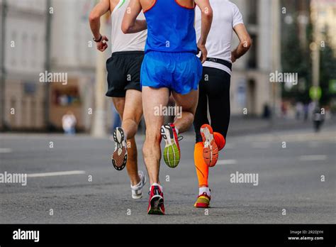 Rear View Three Runners Athletes Running Marathon In City Group Male