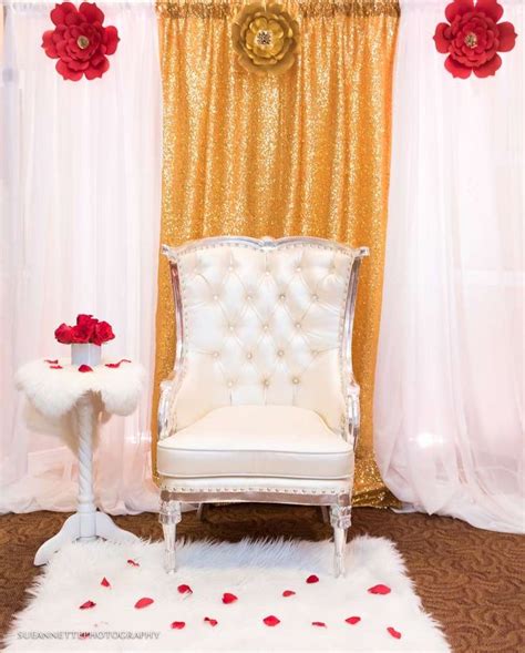 A White Chair Sitting In Front Of A Gold And Red Wall With Flowers On It