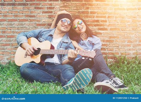 Hipster Man Playing Guitar For His Girlfriend Outdoor Against Br Stock