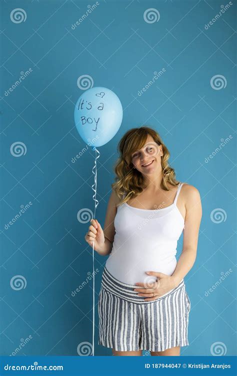 A Pregnant Woman In Front Of A Blue Wall Holds â€œitâ€™s A Boyâ