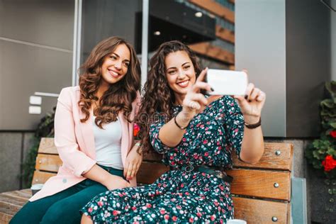 Two Happy Girls Taking A Selfie While Sitting Together Outdoors Stock