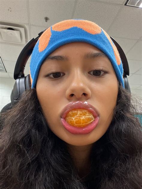 A Woman With Headphones On And An Orange In Her Mouth Is Making A Funny