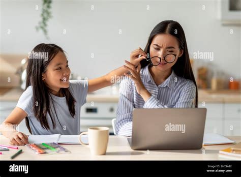 Asian Woman Working On Laptop Computer From Home While Daughter