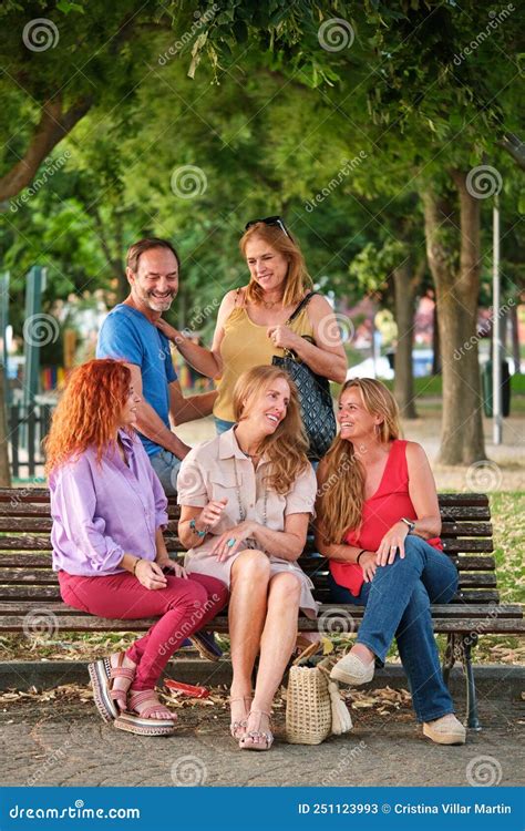 Five Mature Adults Talking And Laughing Sitting On A Bench In A Park