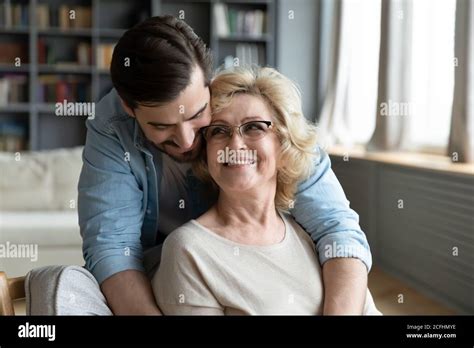 Happy Young Man Hugging Mature Mother Wearing Glasses From Back Stock