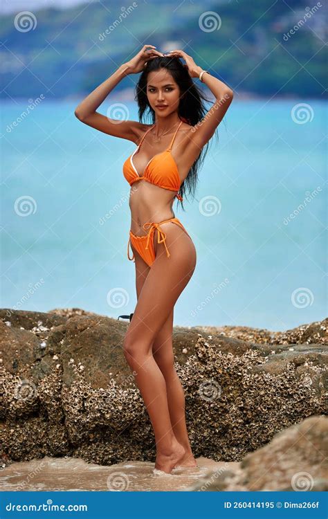 Beautiful Asian Girl In A Orange Bikini Posing On A Beach With Rocks