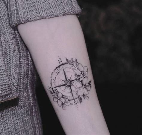 a black and white photo of a compass with flowers on the wrist tattoo ...