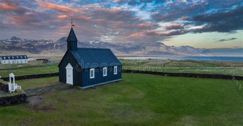 Aerial View Of Black Church In Iceland With Mountains And Water In