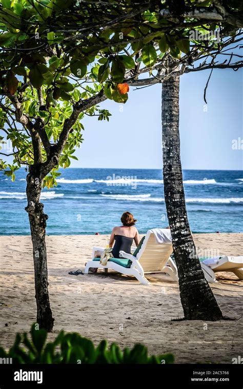 a woman in a swim suit sitting on a beach lounge chair sun bathing on a ...