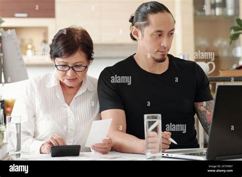 Mature Woman Checking Receipts And Making Calculations When Her Adult Son Paying Bills And