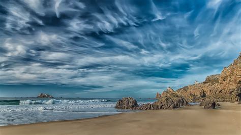 Rock Mountains On Beach Sand And Ocean Waves Under White Clouds Blue