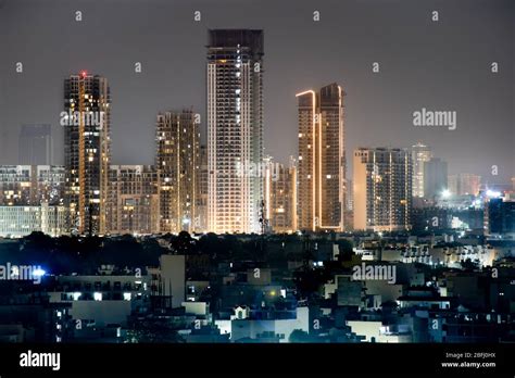 High rise multi story skyscrapers lit up at night with small houses in the foreground at night ...